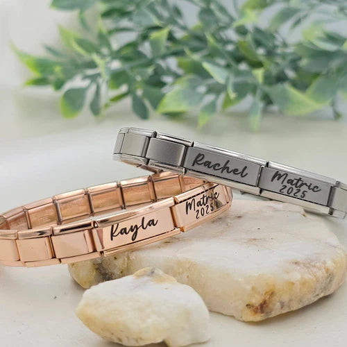 Two bracelets, one rose gold and one silver, with engraved names and dates on a stone surface with greenery in the background.